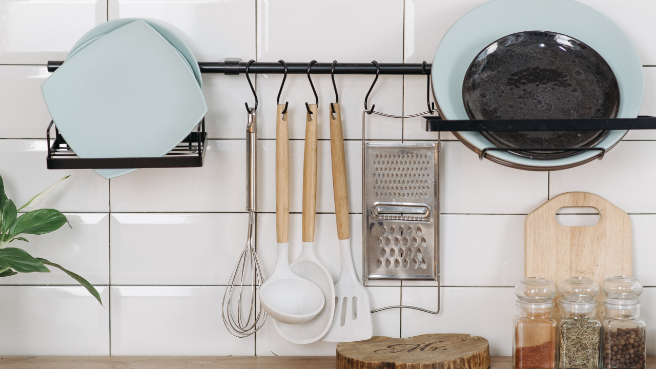 Kitchen utensils, a grater, plates, a cutting board, and spice jars organized against white tile