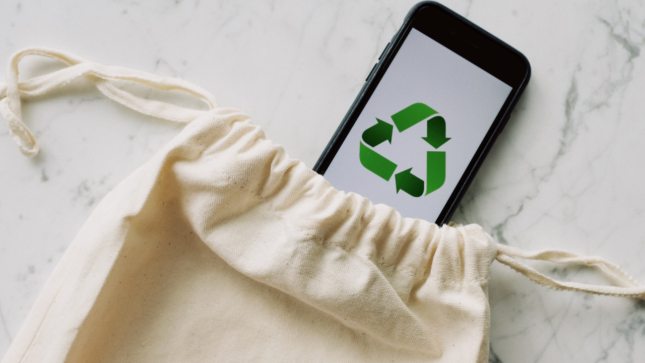 A reusable cloth bag beside a phone showing a recycling symbol