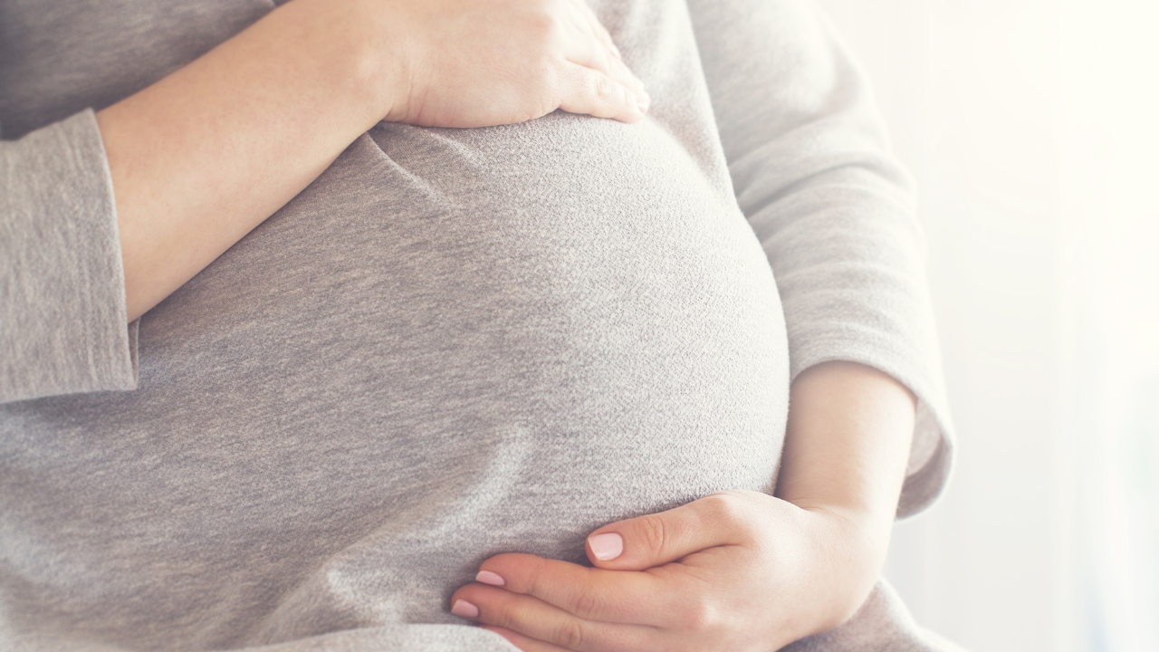 A pregnant person resting both hands on their abdomen