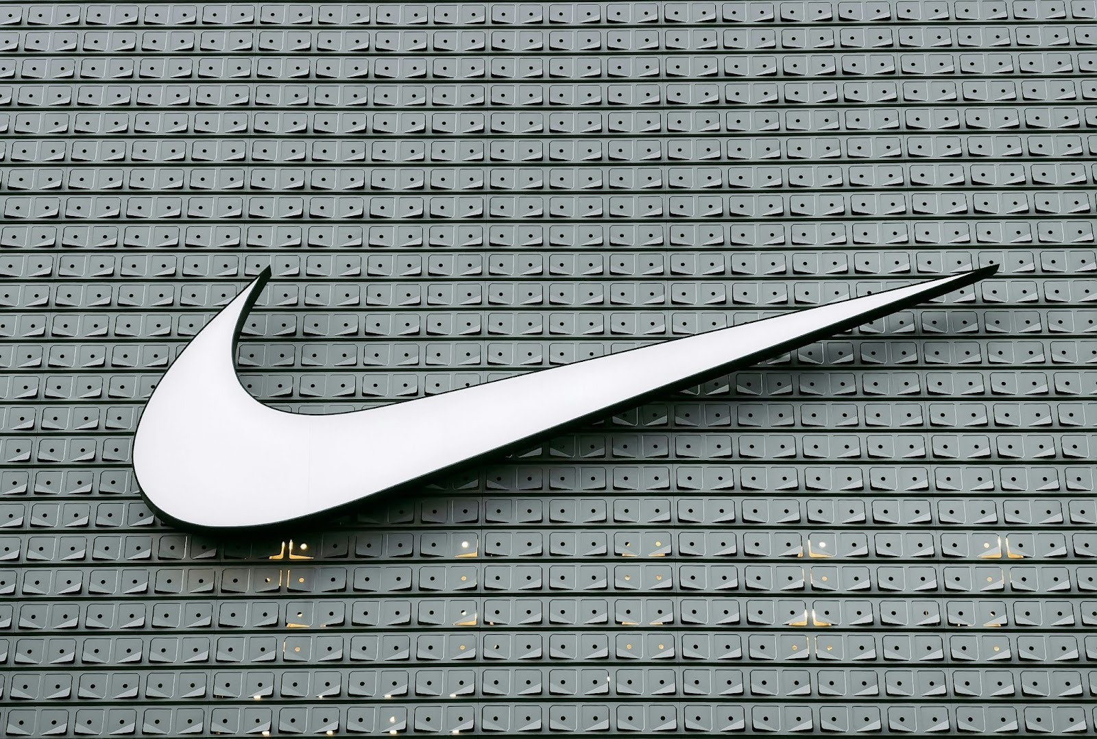 White Nike Swoosh mounted across a wall of gray square panels.