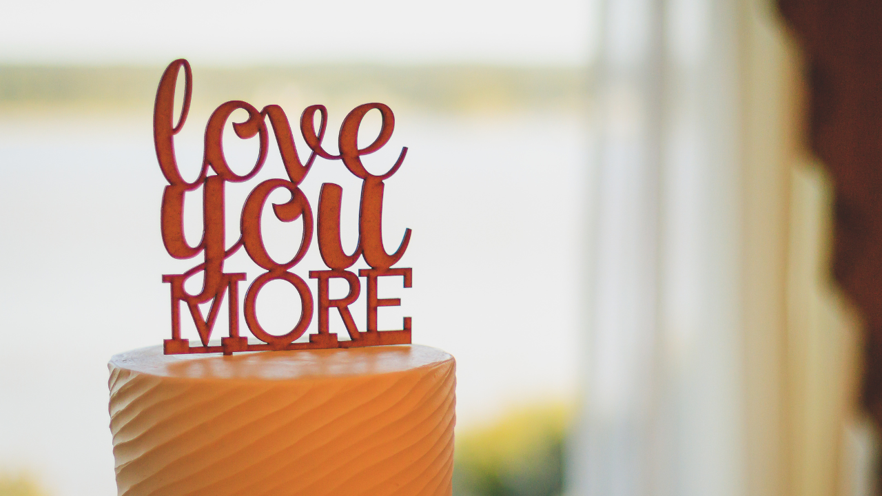Wooden love-you-more topper on a frosted cake