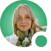 Cartoon avatar of a smiling woman with light skin, brown hair, green eyes, and pink lipstick wearing a green top.