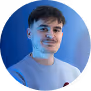 Portrait of a person with short hair and a light blue shirt against a blurred background.