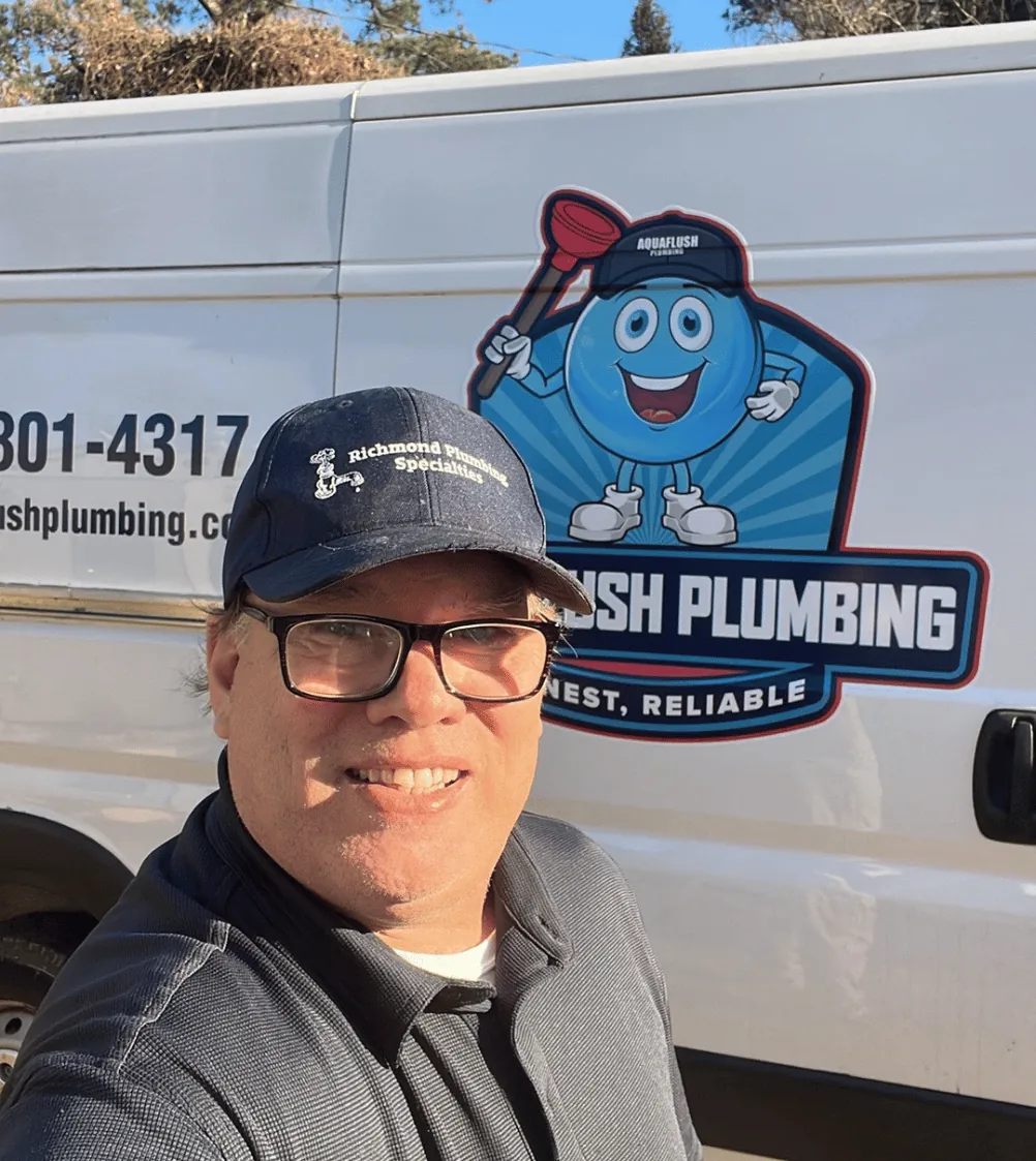 Smiling man wearing glasses and a Richmond Plumbing Specialties cap standing in front of a white van with the Aquaflush Plumbing logo.