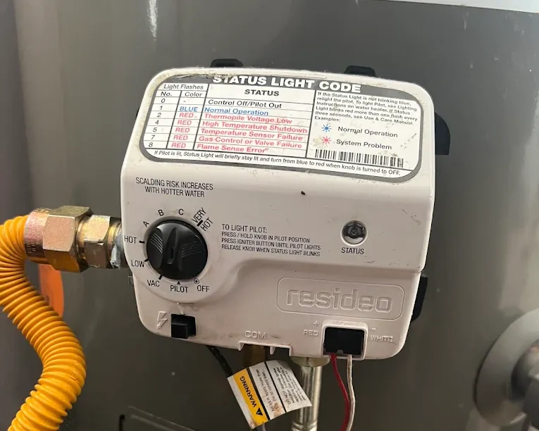 Close-up of a Resideo water heater control panel with a rotary switch, status light codes, and a warning about scalding risk with hotter water.