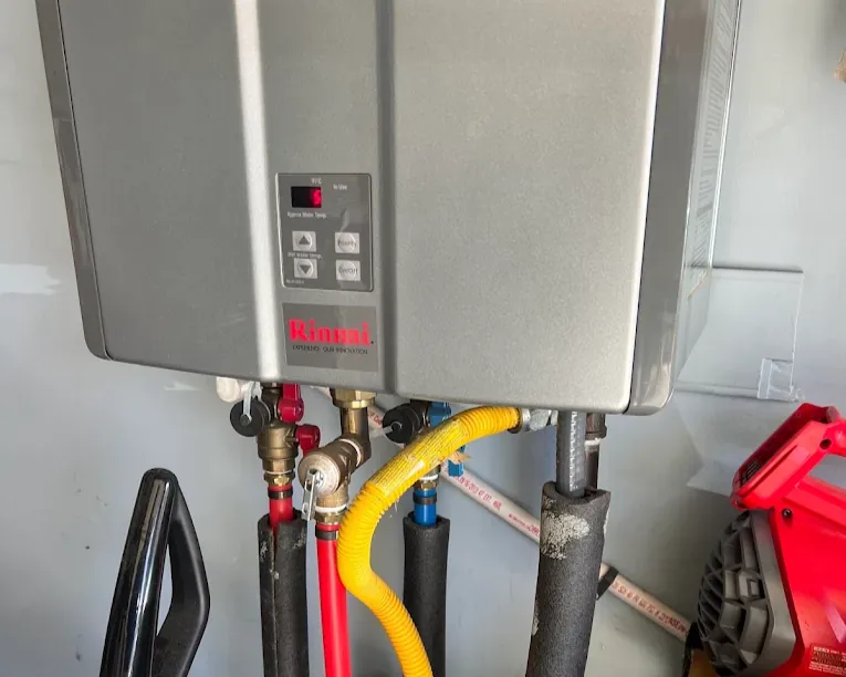 Rinnai tankless water heater with red, yellow, and blue pipes connected underneath.