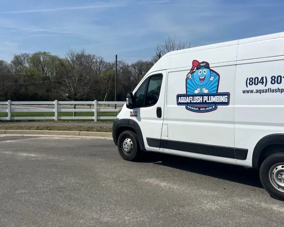 White Aquaflush Plumbing van parked on a road with trees and a white fence in the background.