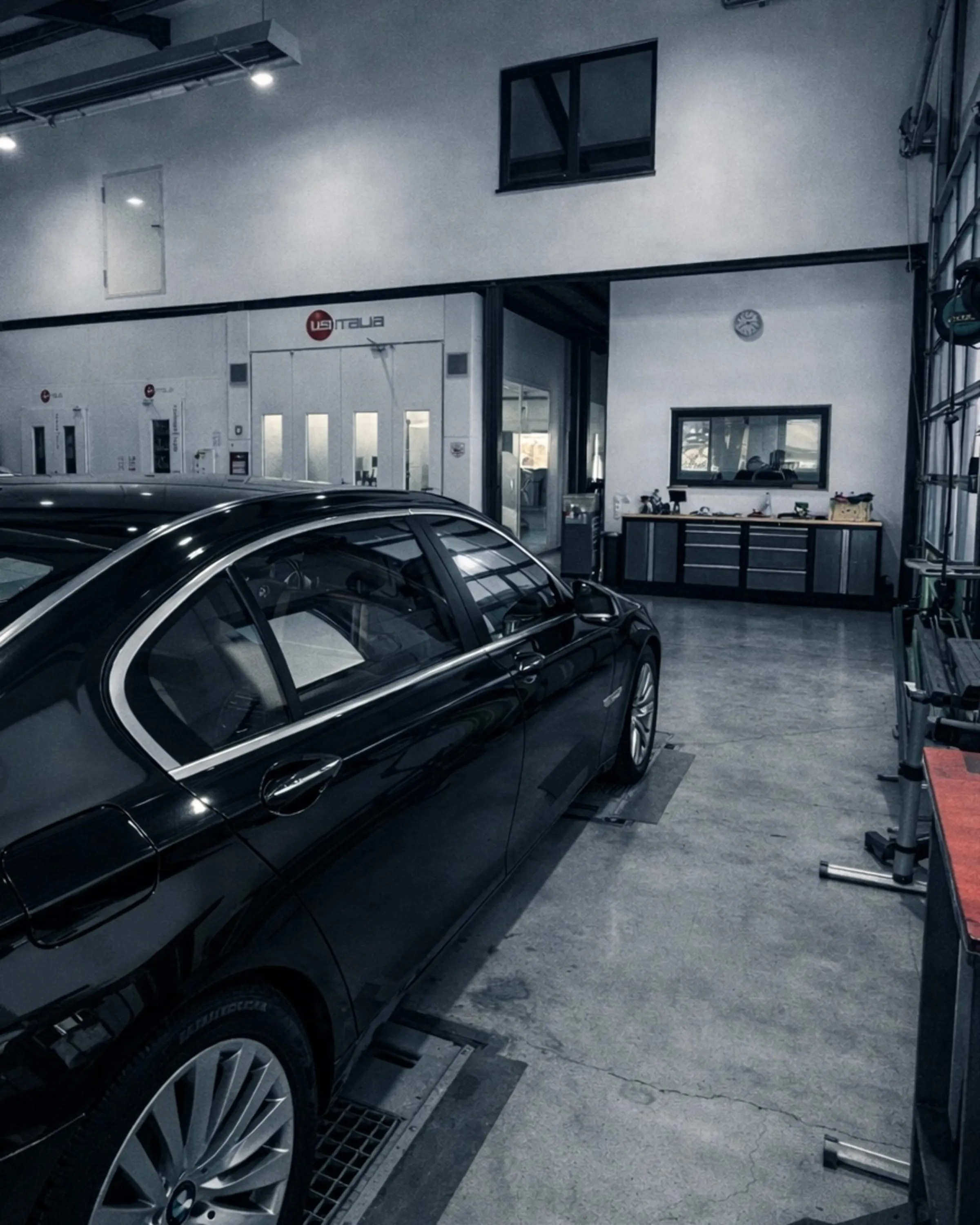 Schwarzes Auto in einer modernen Autowerkstatt vor weißen Lackierkabinen.