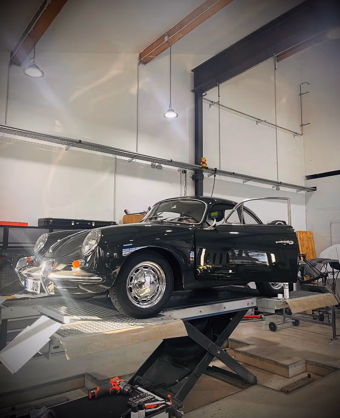 Schwarzes klassisches Auto auf Hebebühne in moderner Werkstatt mit geöffneter Tür.