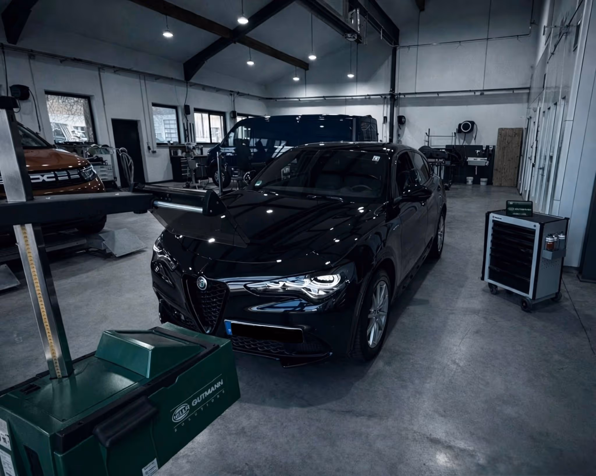 Schwarzes Alfa Romeo Auto in einer Werkstatt mit Fahrzeugprüfgerät davor.