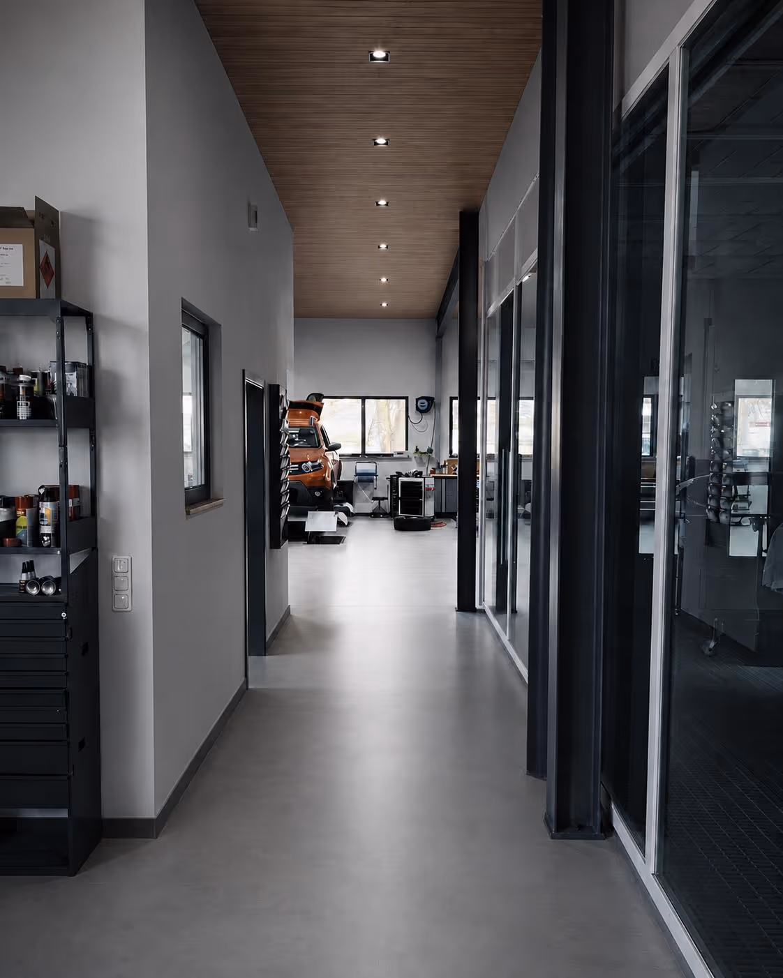 Moderner, sauberer Flur mit Regal, großen Fenstern und orangenem Auto am Ende der Garage.