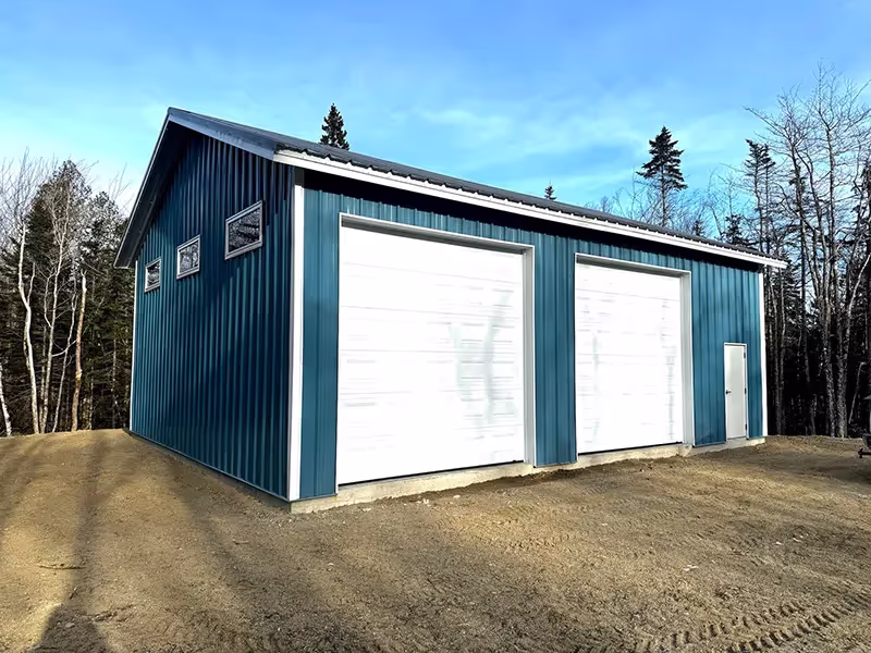 Blue steel building with two large white garage doors and a side door
