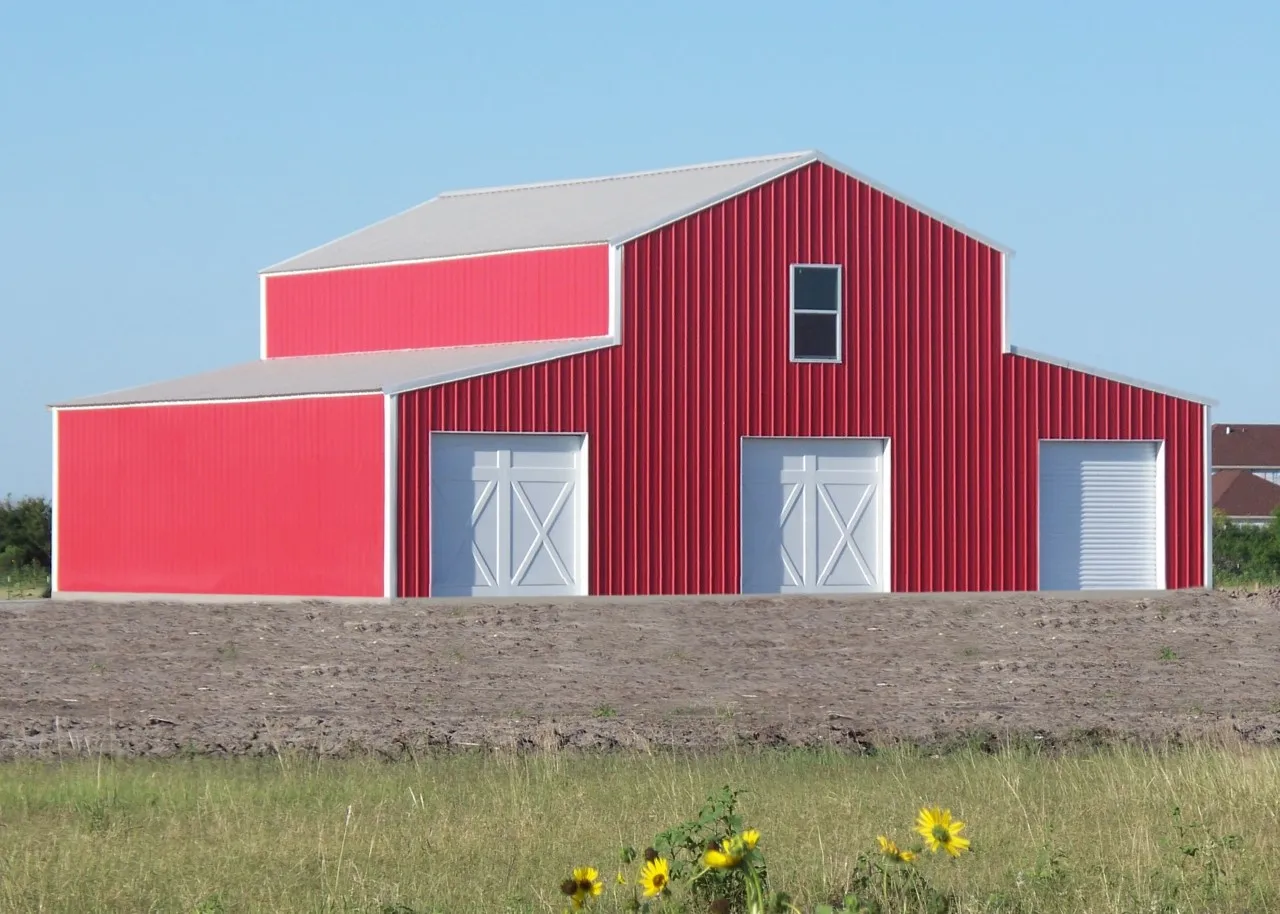 Red steel farm barn with white doors under a clear blue sky
