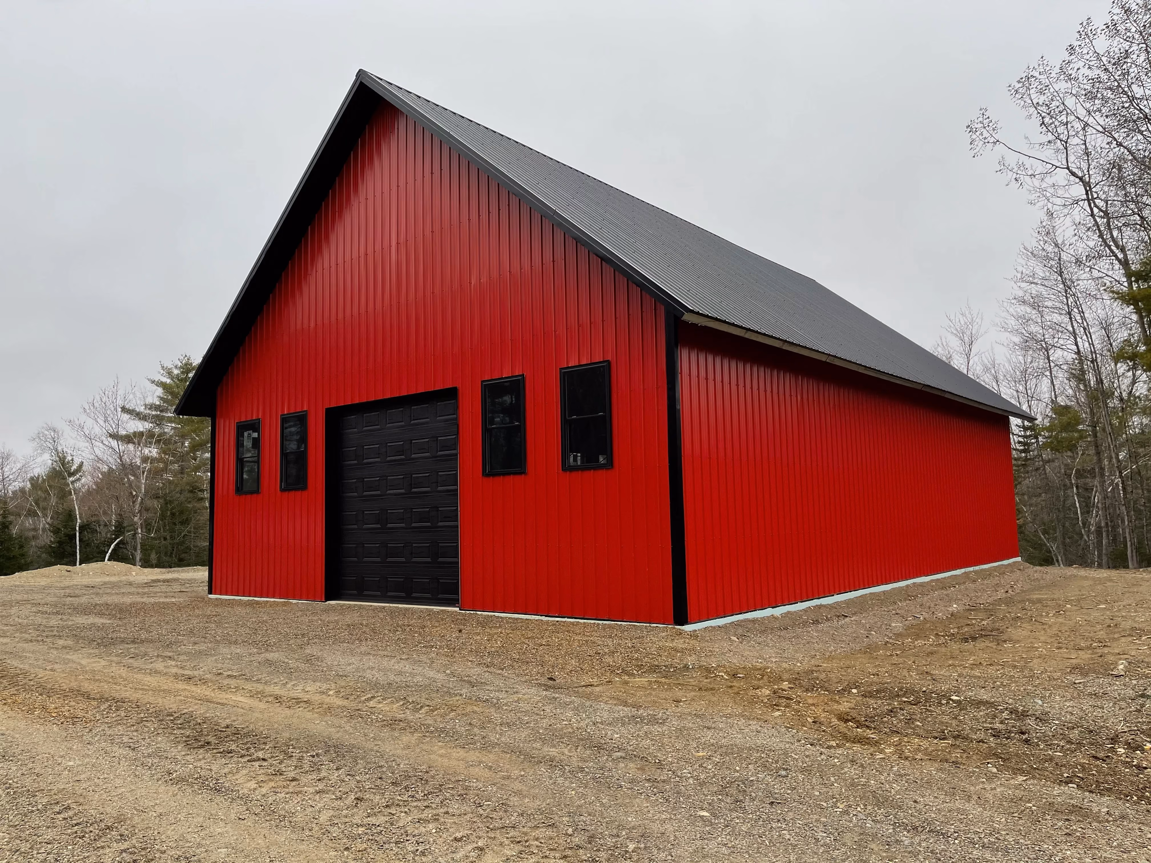Large red steel-framed metal building with a black roof, black garage door, and black-framed windows.