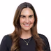 Smiling woman with long brown hair wearing a black top and a necklace against a plain white background.