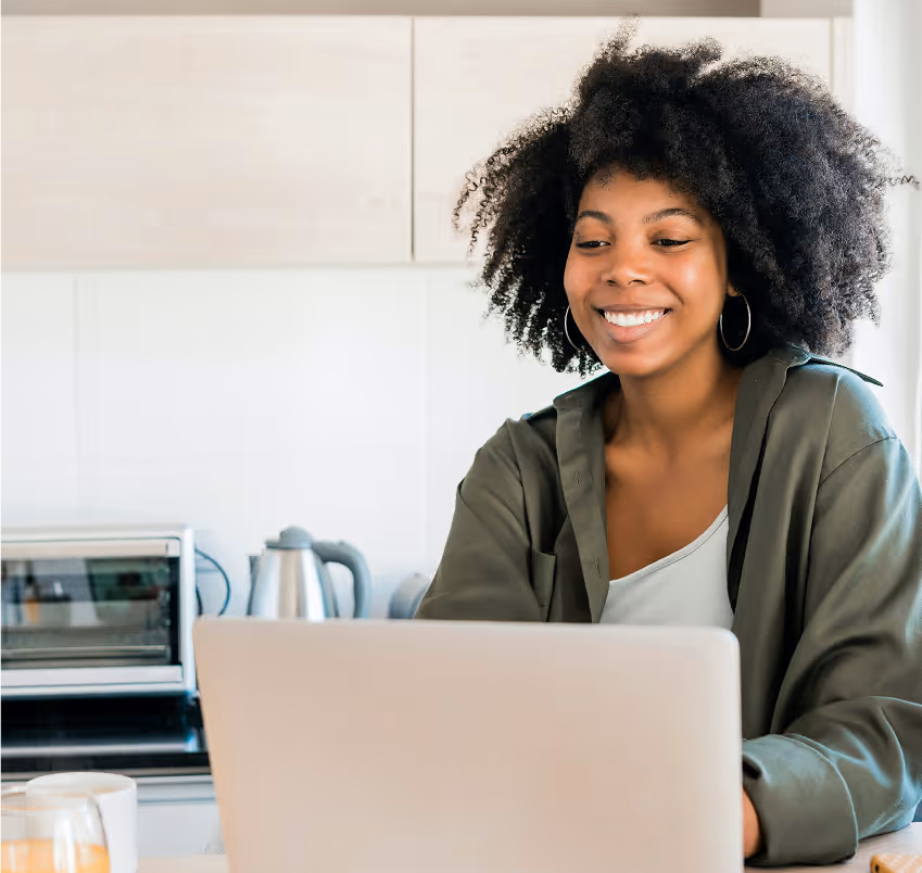 Smiling woman with curly hair using a laptop in a kitchen with a floating chat box from Vanessa, RDN asking about goals, feelings about food, and typical day of eating.
