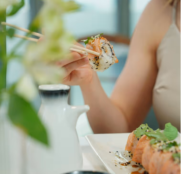 Person using fork to eat pasta with salad, bread, and pizza on table; overlay text advises to get around 25g of protein at lunchtime.
