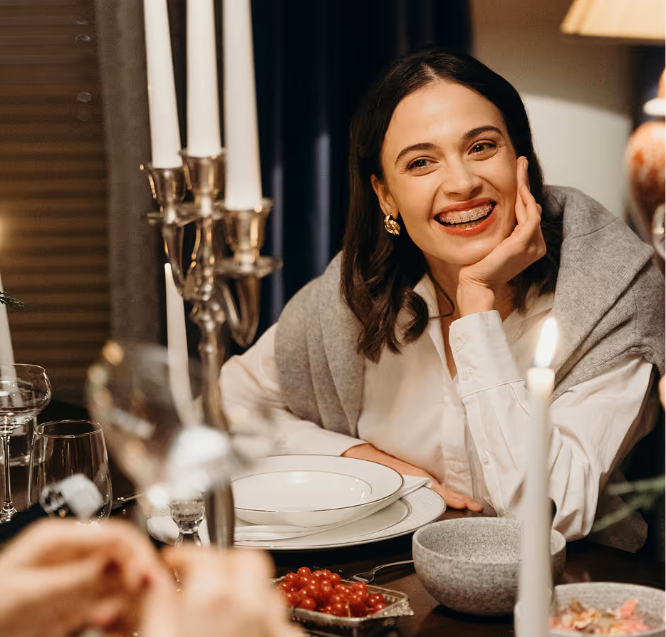 Smiling woman with braces sitting at a candlelit dinner table with plates and bowls, a chart showing a habit loop with cue, routine, and reward is overlaid.