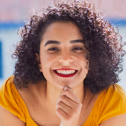 Smiling woman with curly brown hair wearing a green and white patterned shirt against a plain background.