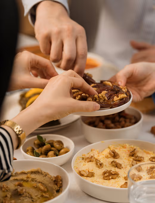 Hands reaching for a plate with dates topped with walnuts among bowls of nuts and snacks on a table.