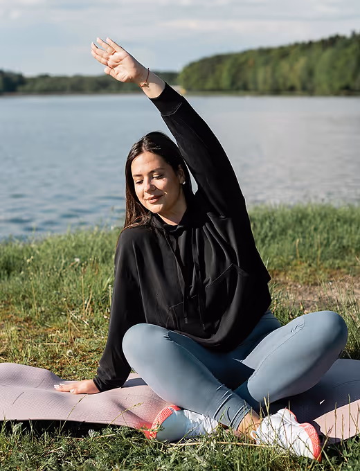 Woman with curly hair sitting cross-legged on a yoga mat in meditation posture with eyes closed and hands pressed together at chest.