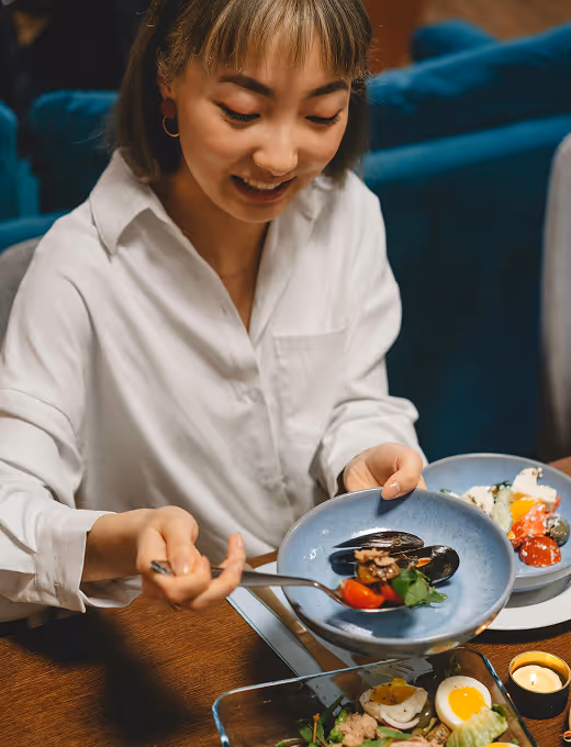 Woman in white shirt smiling and serving food from a dish at a dining table.