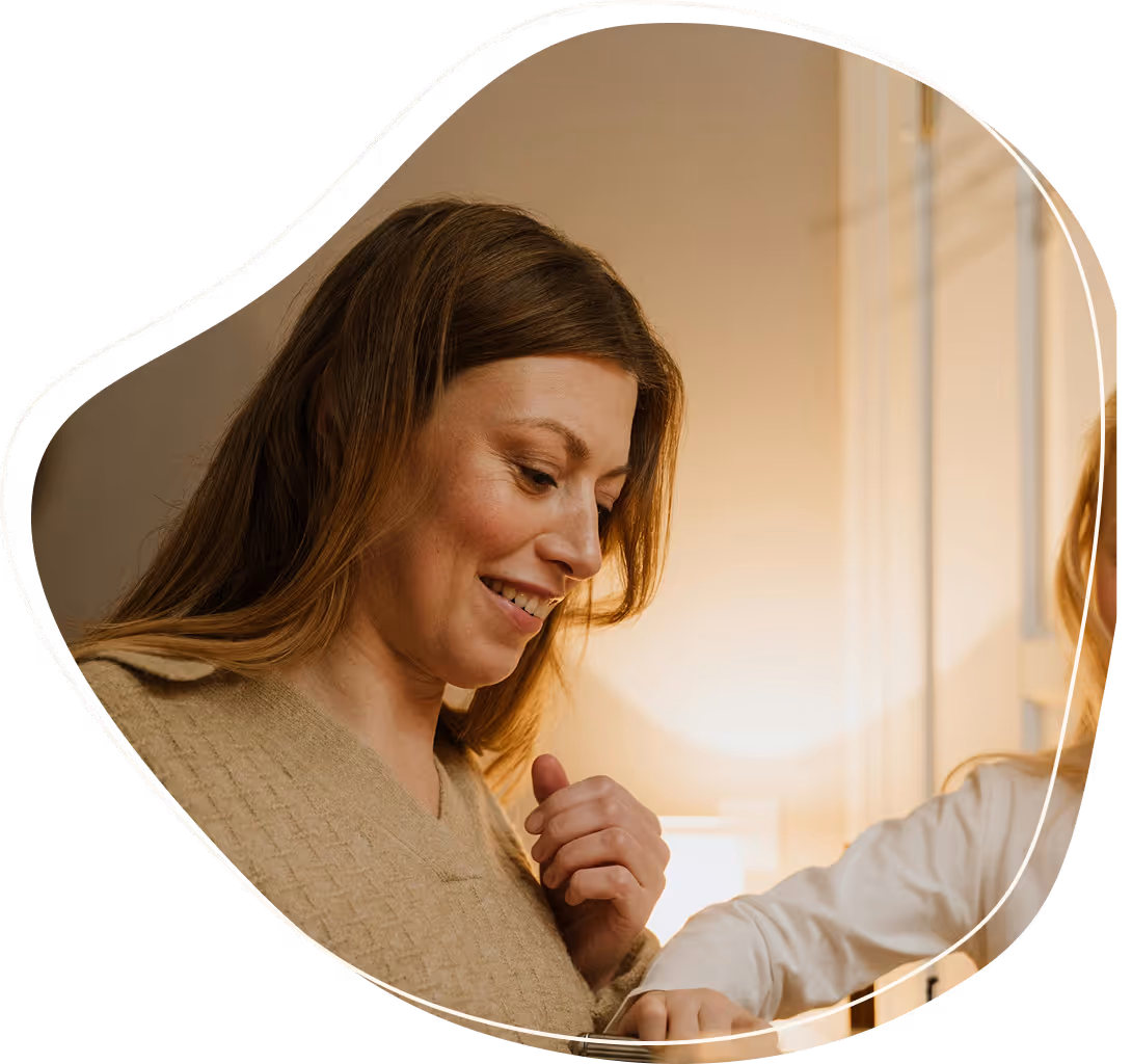 Smiling woman looking down at a child's hand reaching towards her sweater in a warmly lit room.
