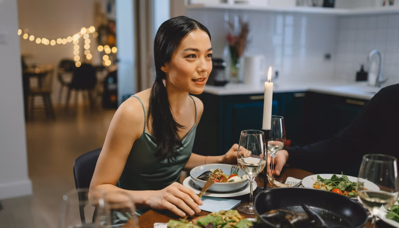 Woman in a green dress sitting at a candlelit dining table with dishes and glasses of white wine.