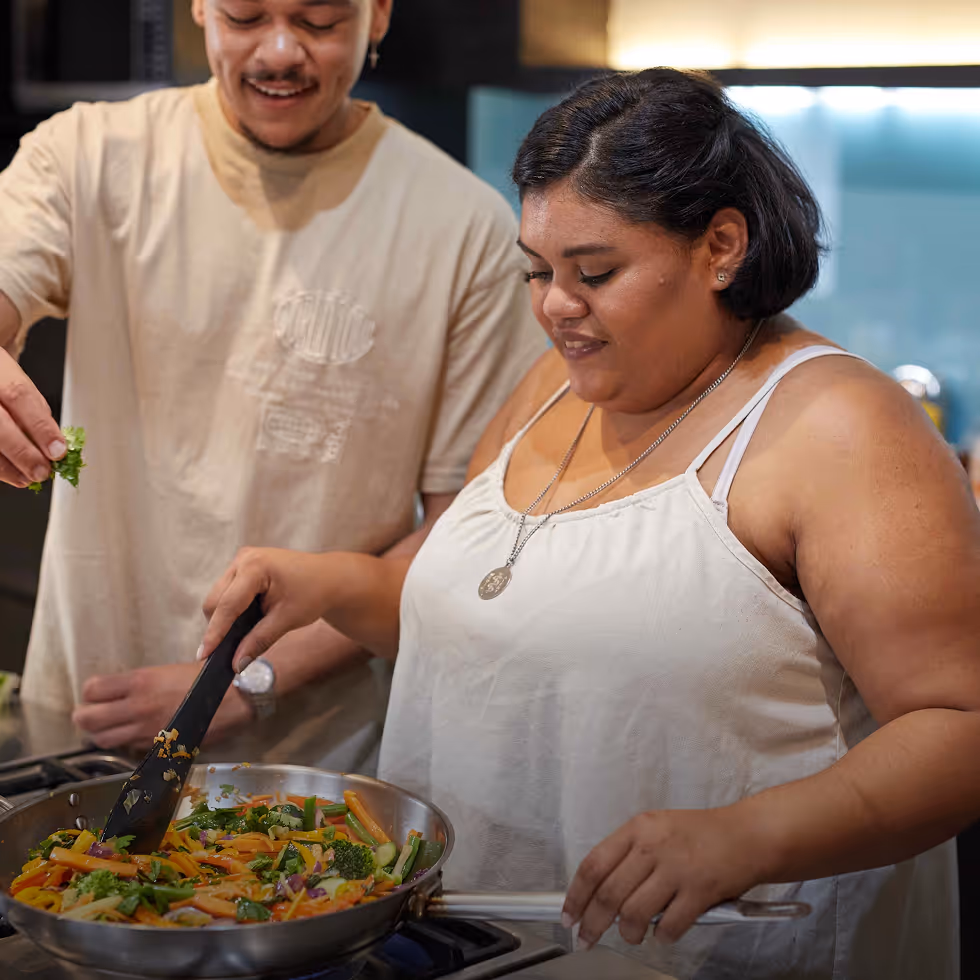 Two people cooking together in a kitchen, stirring a pan filled with colorful vegetables.
