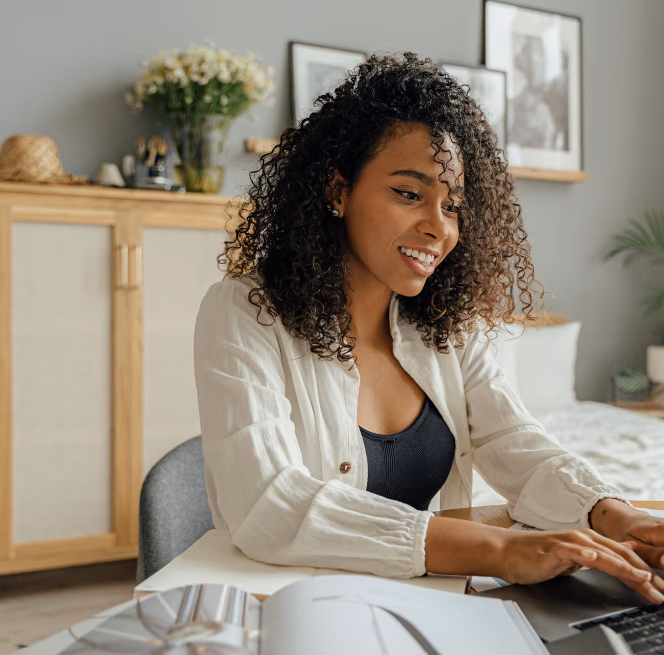 Smiling woman talking on a smartphone while looking at an open Apple laptop on a couch.