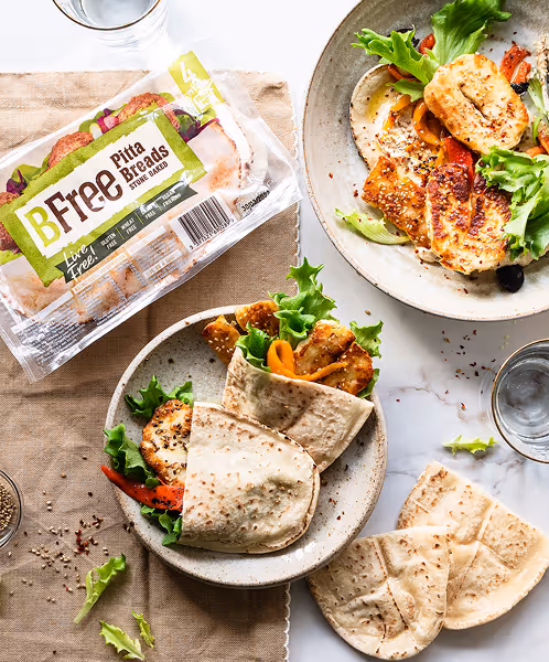 Plates with grilled chicken wraps and salad, beside a package of BFree Pitta Breads on a table.