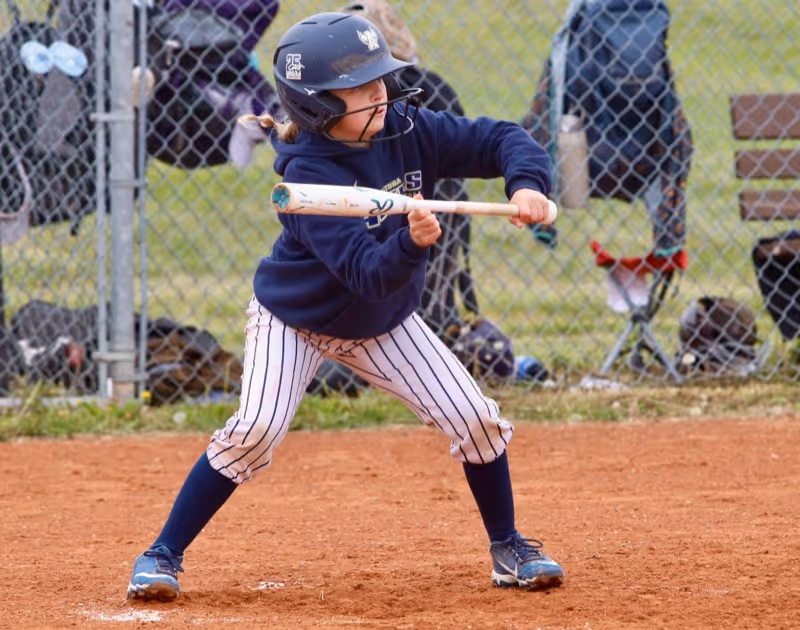 Young player at bat wearing helmet, holding bat, in full uniform with cleats