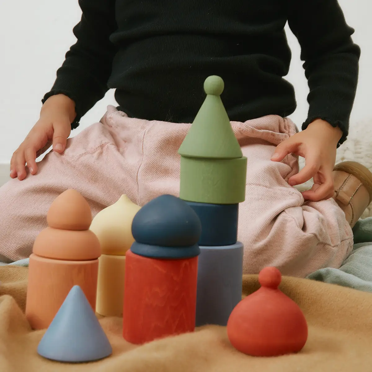 Child sitting with colorful wooden stacking toys arranged on a soft surface.