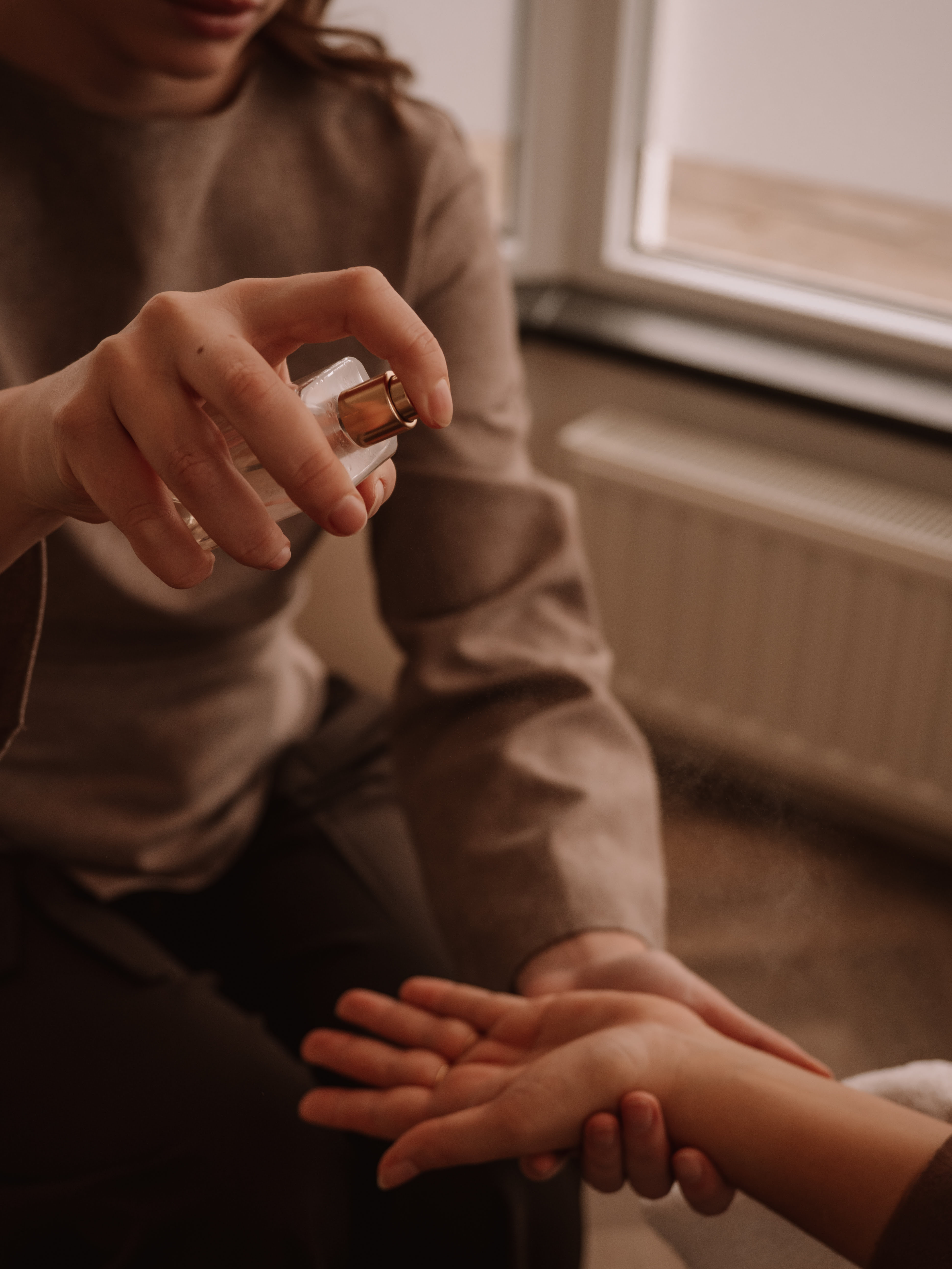 Person spraying a liquid from a small bottle onto another person's wrist indoors.