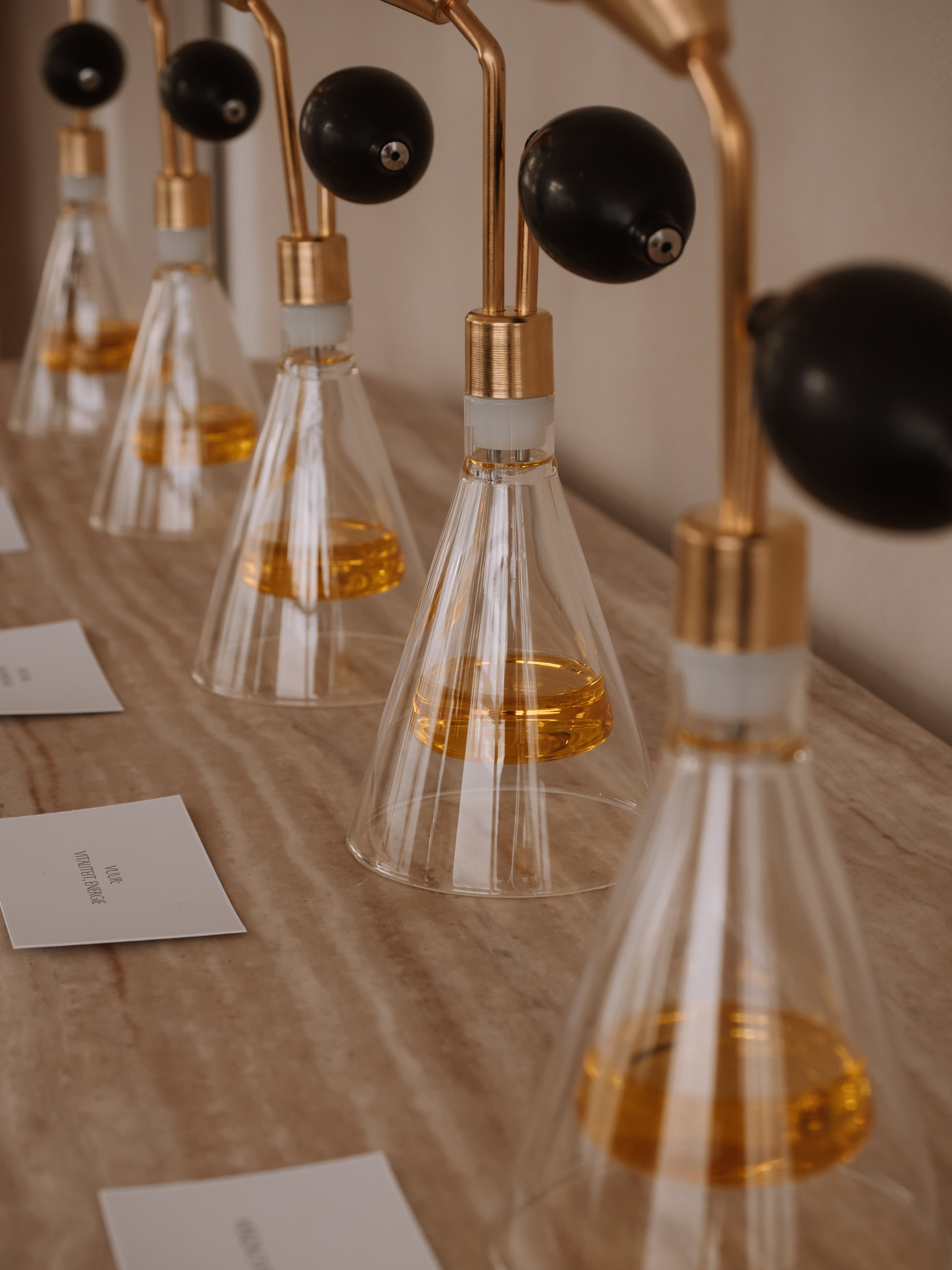 Row of vintage glass perfume atomizers with amber liquid on a beige marble surface.