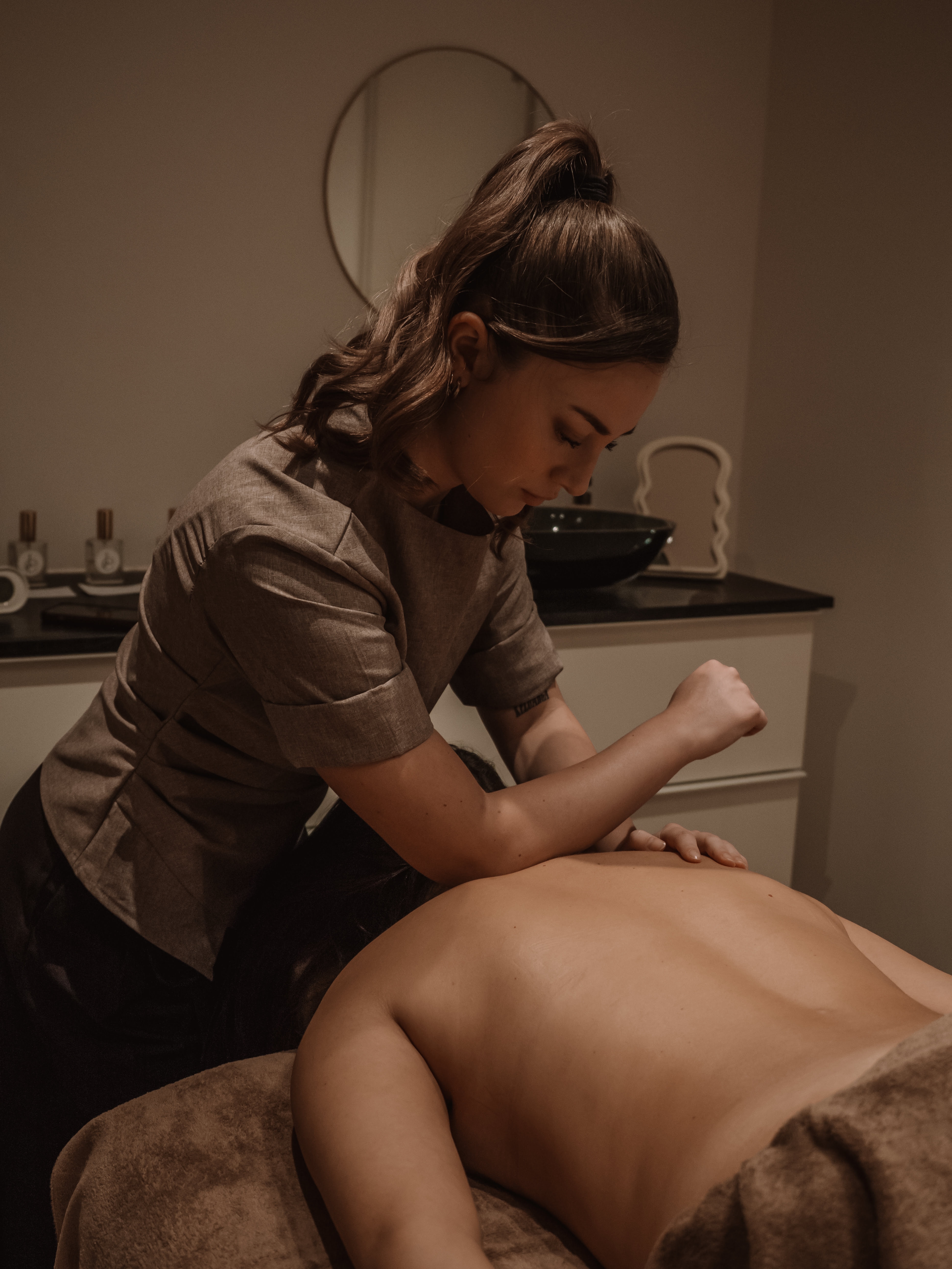 Therapist giving a deep tissue massage to a person lying face down on a massage table in a dimly lit room.