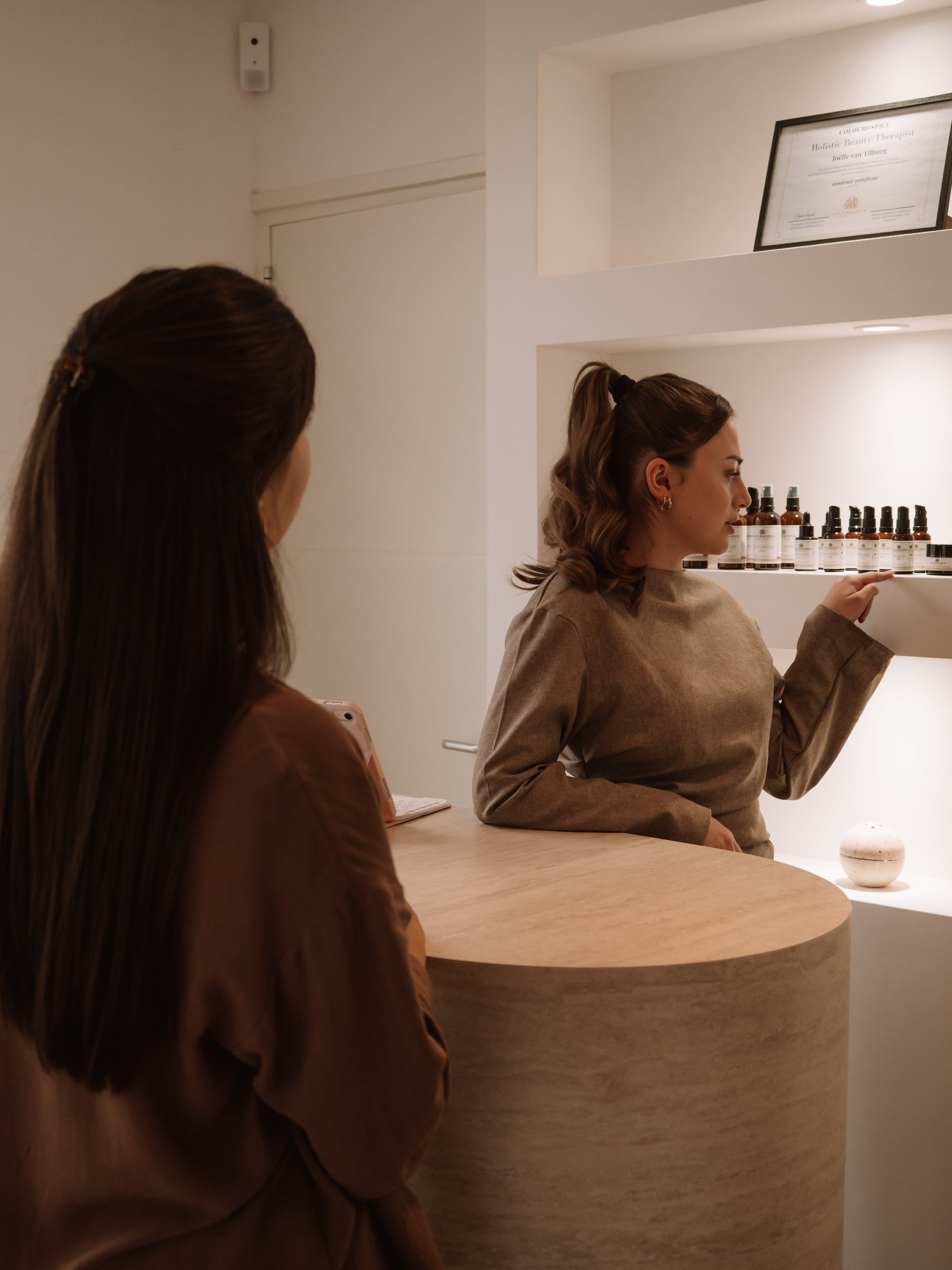 A woman behind a counter showing skincare products to a customer in a softly lit boutique.