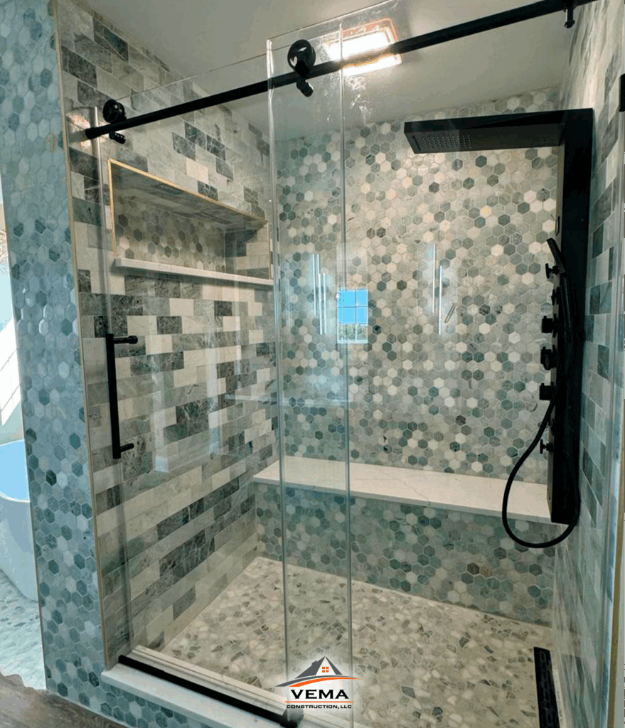 Modern shower with glass sliding doors, hexagonal tile pattern on walls, built-in bench, and black rainfall showerhead.