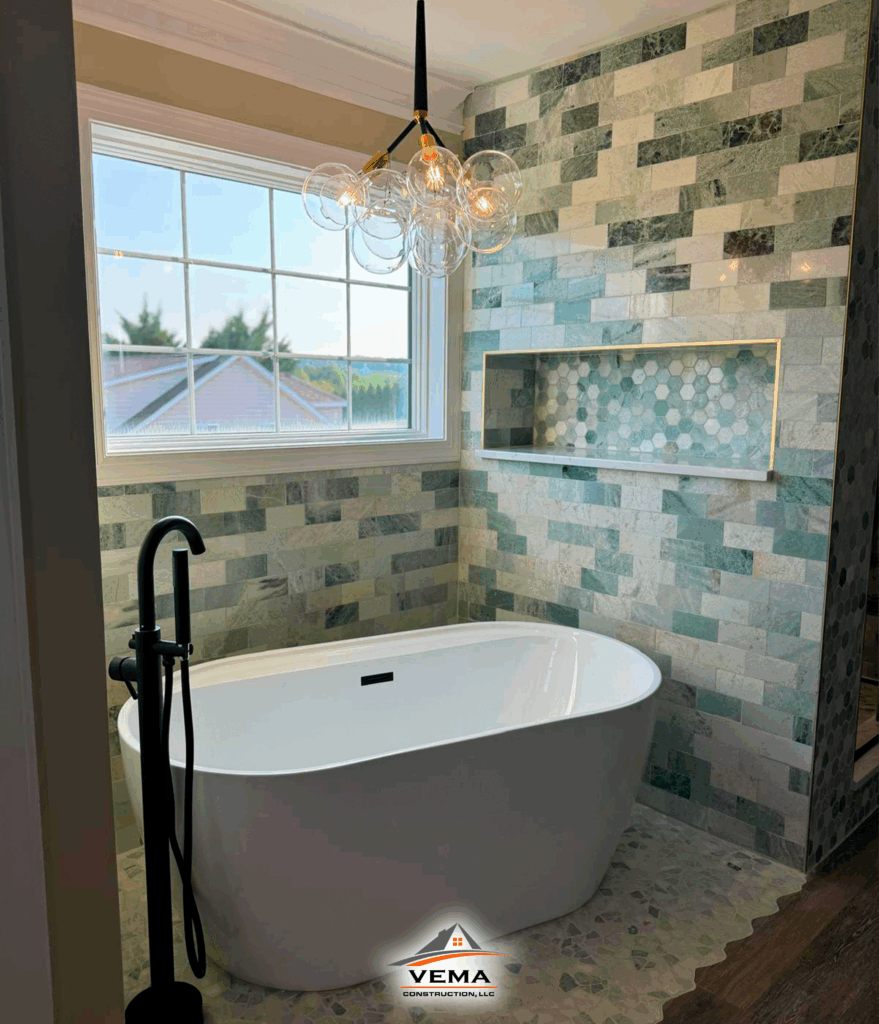Modern bathroom with a white freestanding bathtub, black floor-mounted faucet, mosaic green and gray tiled walls, hexagonal tile niche, and a glass bubble chandelier.