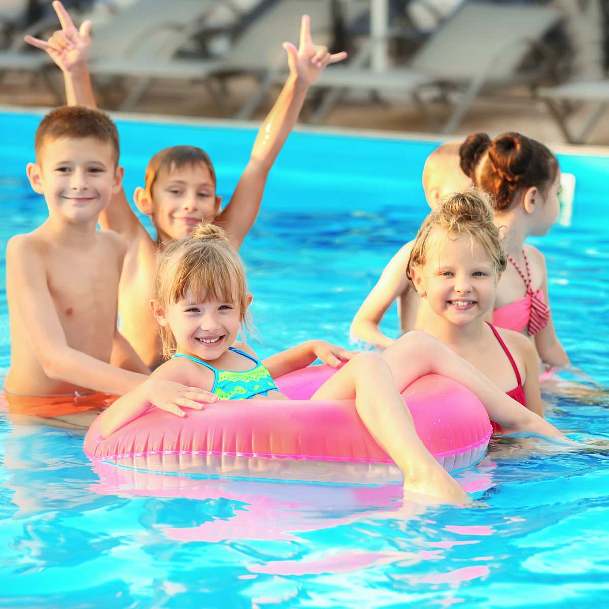 Group of smiling children playing and relaxing in a swimming pool with a pink inflatable ring.