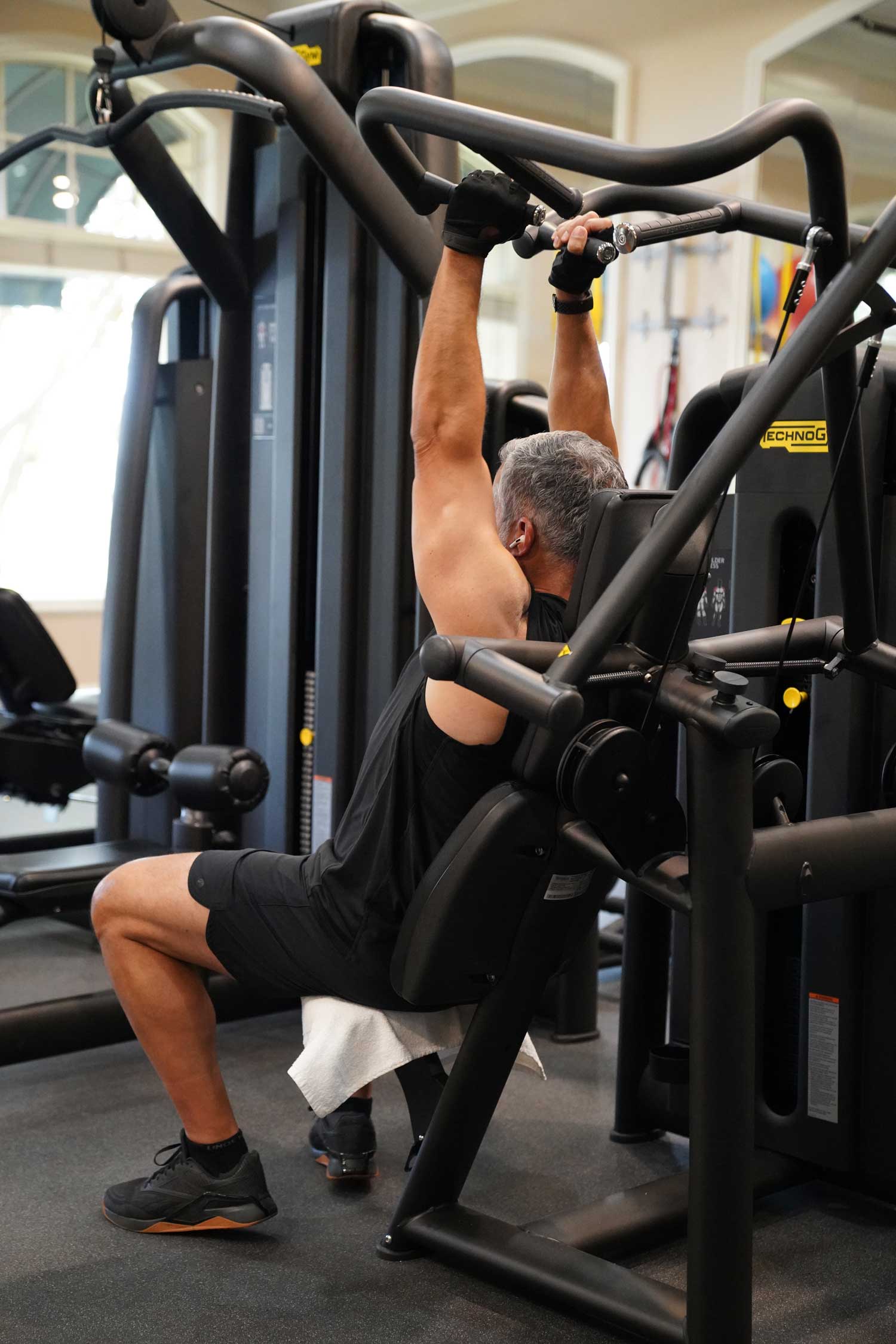 Man in black workout attire using a gym machine for a lat pulldown exercise.