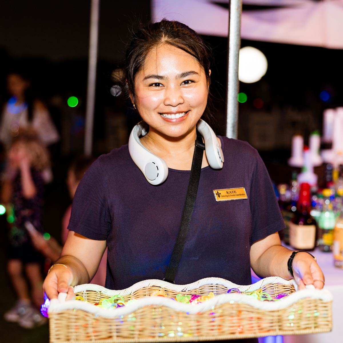 Smiling woman wearing a navy shirt and headphones around her neck holding a wicker basket at an event.