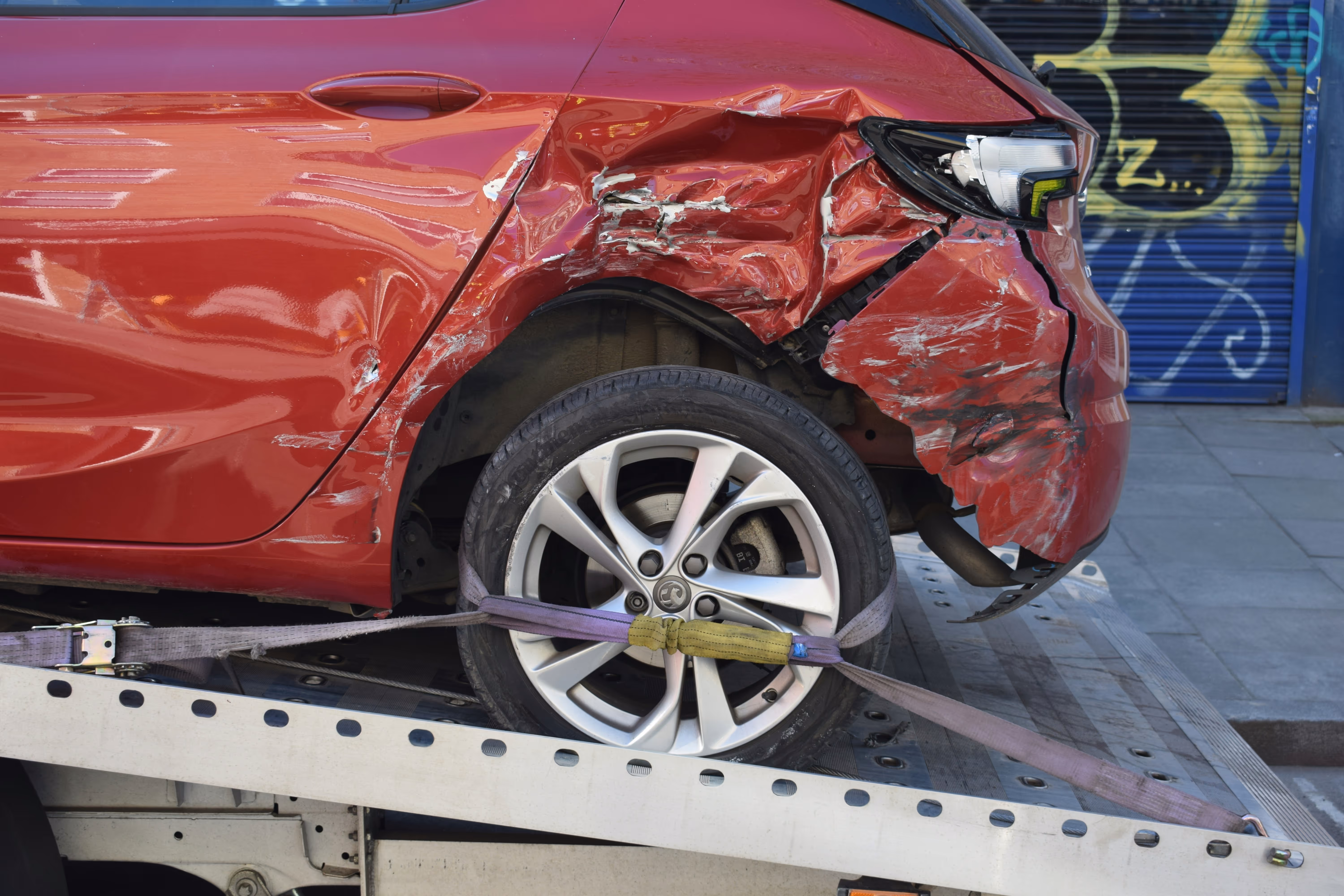 A heavily damaged red car being transported on a tow truck, illustrating TrueSpan Group’s dedicated claims advocacy and support following a major auto accident.