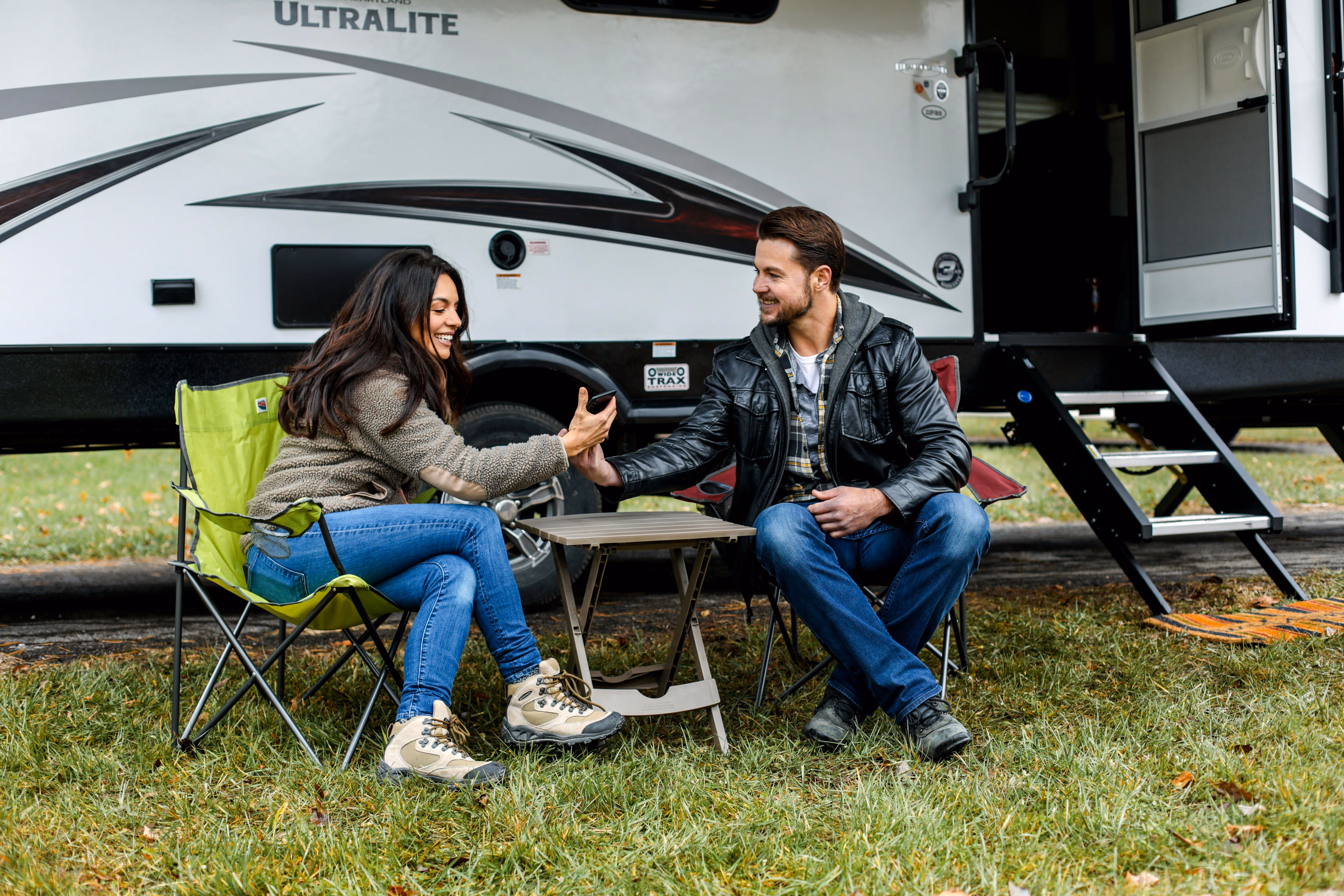 A happy couple sitting in camping chairs outside their travel trailer, representing TrueSpan Group’s specialized RV insurance for motorhomes and campers.