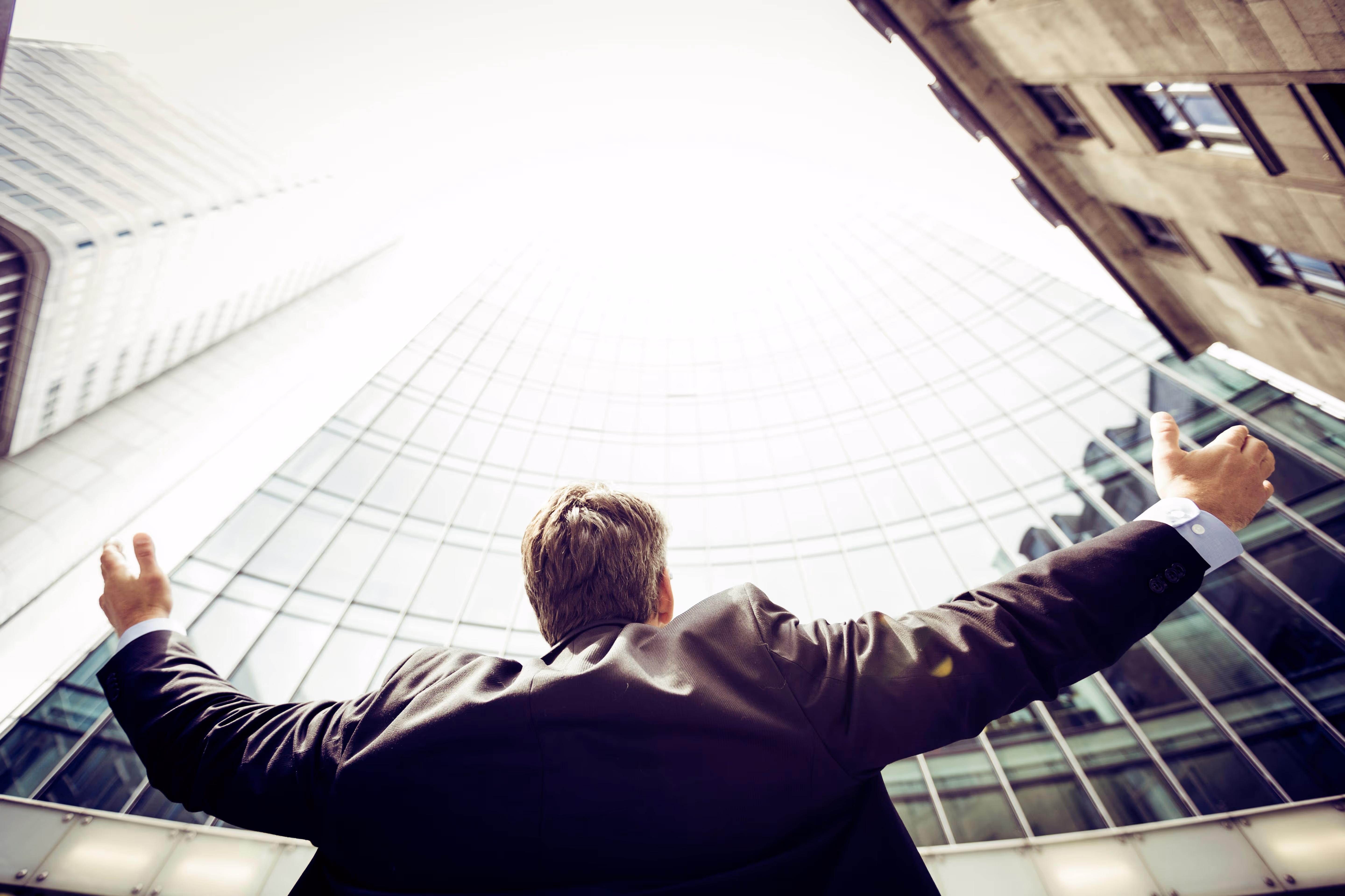 A professional man looking up at modern glass skyscrapers, symbolizing the success and real results TrueSpan Group achieves for business insurance clients.