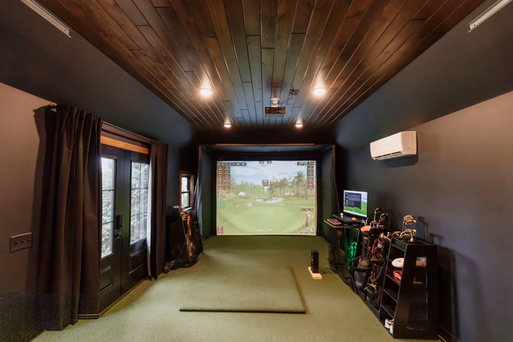 Long golf simulator room with projector screen and turf