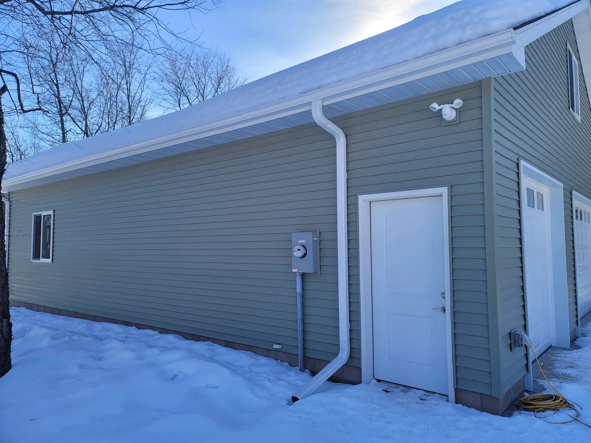 Side of gray garage with white door in snow