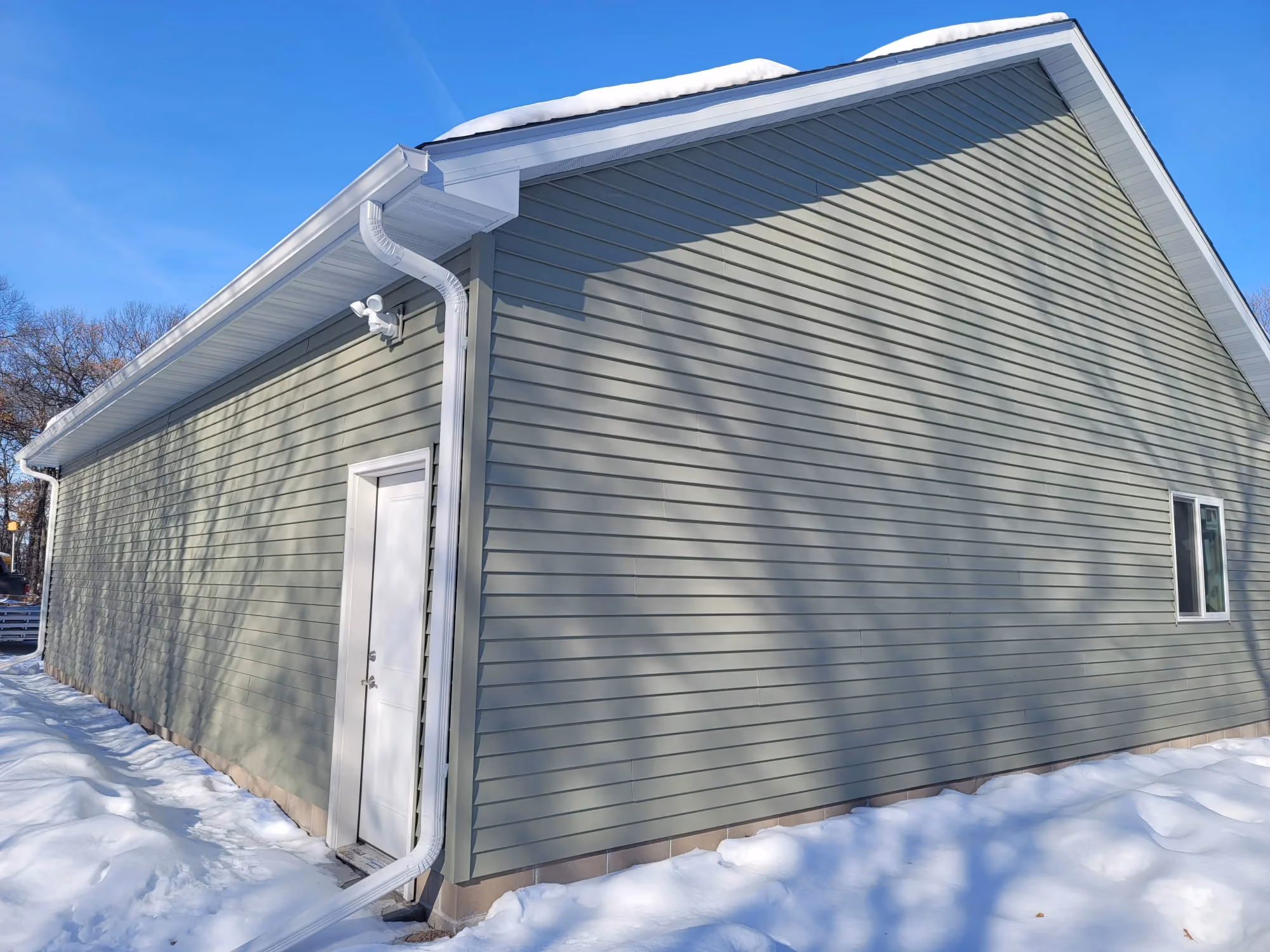 Gray garage side wall with downspout in snow