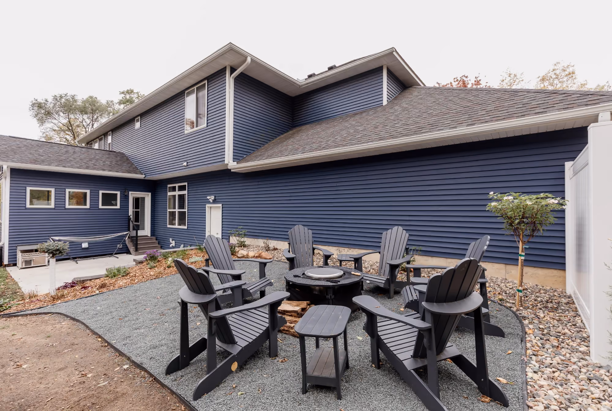 Outdoor dining set on gravel patio outside blue house