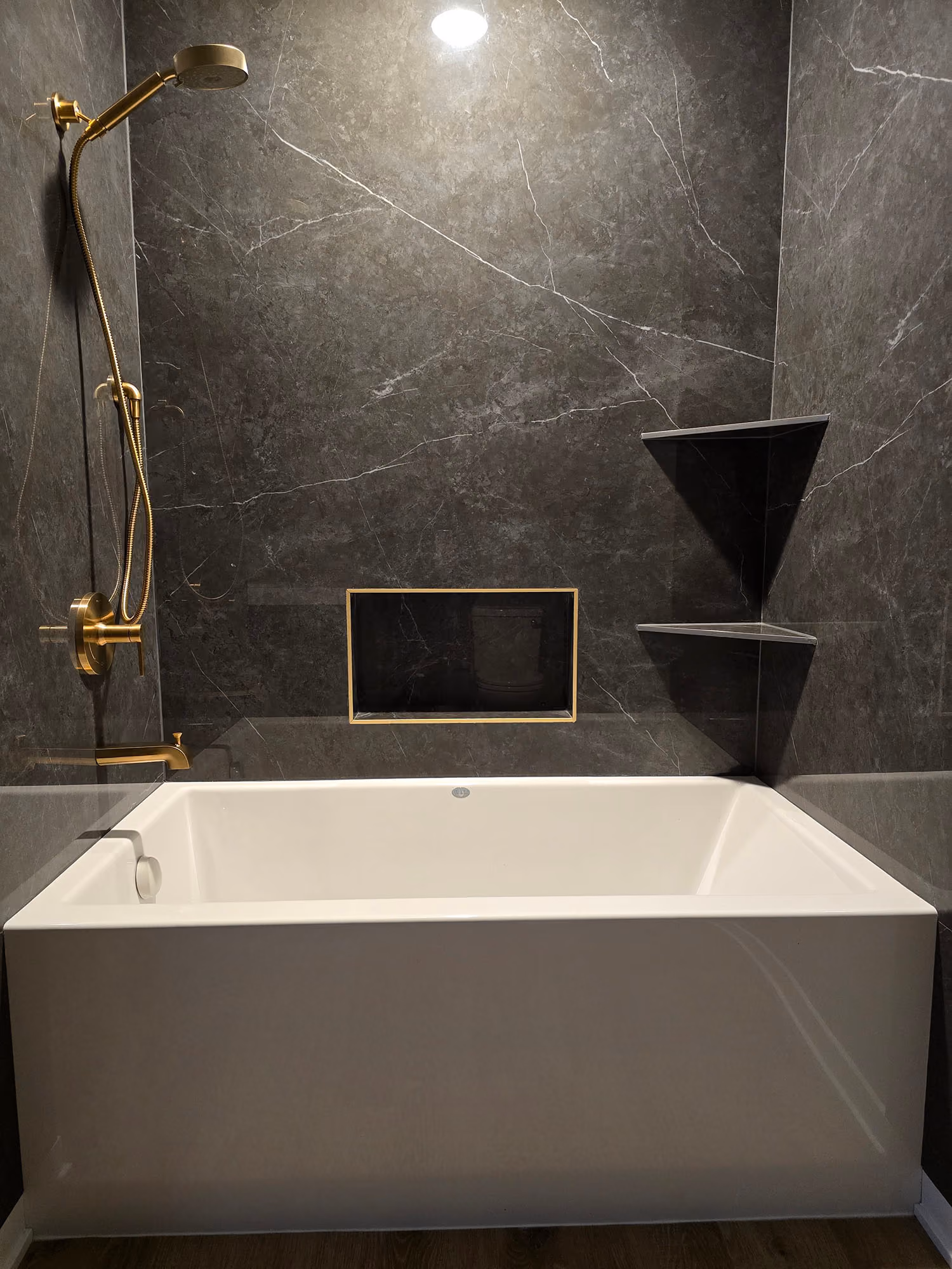 Bathtub with dark tile surround and brass shower fixture